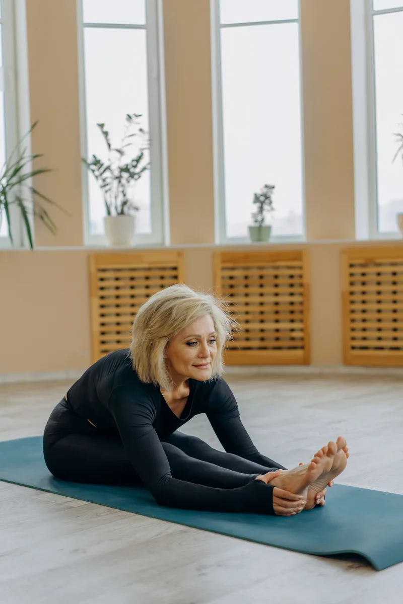 A woman stretching on a teal exercise mat in a bright room.